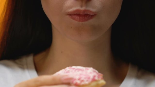 Attractive sugar addicted woman eating glazed donut, risk of diabetes, close up