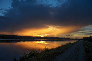 Sunset on the river. Single lane road leading through landscape.