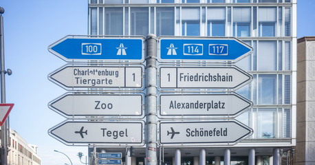 Signposts with arrows show the main directions of Berlin, Germany. Blue sky and building background.