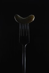 pickled gherkin on a fork on black background