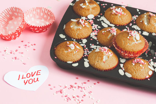 Muffins with sweet heart decor, pink background, paper heart with text I love you, Valentine's day