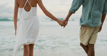 Beautiful couple holding hands on a tropical beach at sunset, mixed race