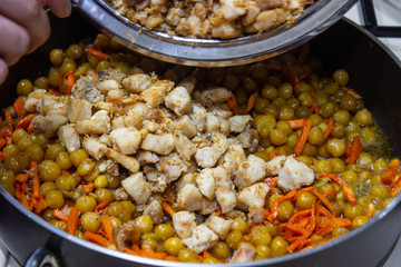 Chopped chicken in a pan with chopped carrots and peas