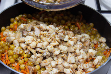 Chopped chicken in a pan with chopped carrots and peas