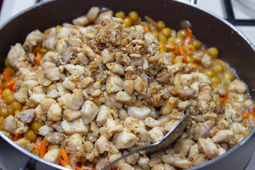 Chopped chicken in a pan with chopped carrots and peas