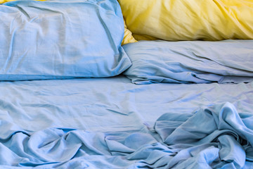 Messy unmade bed  with blue sheets and blue and yellow pillows