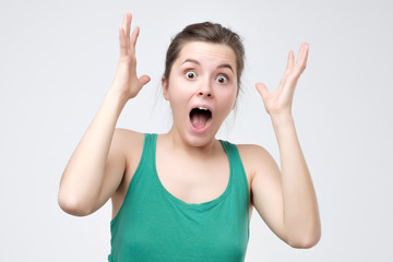 Surprised young woman in green clothes shouting shocked with great news.