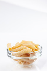 Raw feathers macaroni in bowl. Italian pasta close up on the white background