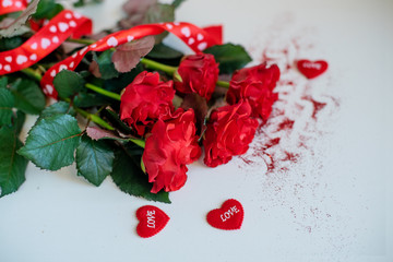 Rose flowers, red ribbon and decorative hearts on light wooden background