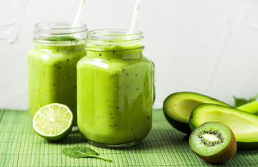 Green smoothie on green background made by avocado, lemon and kiwi.