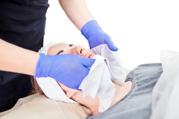 Obraz premium The process of removal a cosmetic cream from the face of a young woman. Hands of the cosmetologist in gloves. Facial skin care. Peeling