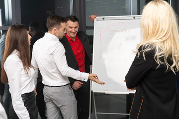 Group of young confident bisiness people analyzing data using office board