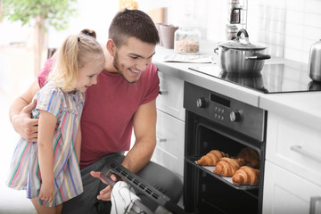 Little girl watching her father bake croissants in oven indoors
