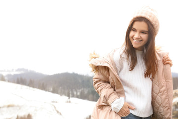 Young woman in warm clothes near snowy hill, space for text. Winter vacation