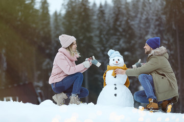 Couple making snowman near forest. Winter vacation