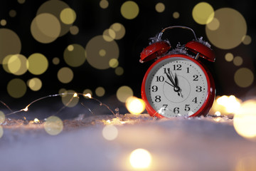 Fototapeta na wymiar Alarm clock and Christmas lights on snow against blurred background, space for text. Winter night