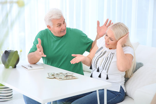 Mature couple with money and piggy bank having argument at table