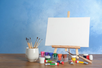 Wooden easel with blank canvas board and painting tools for children on table near color wall....