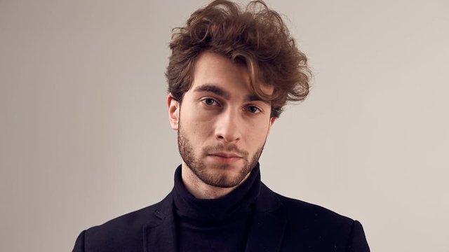 Fashion portrait of handsome elegant man with curly hair wearing suit and glasses on gray background in studio
