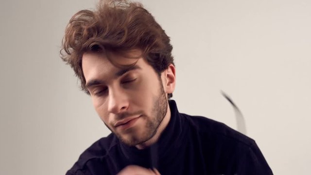 Fashion portrait of handsome elegant man with curly hair wearing black turtleneck and glasses on gray background in studio