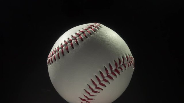 Sports and games. Close up of a white leather baseball with red stitching rotating and moving forwards and backwards.
