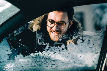 close up portrait of man using scraper for cleaning out car windows. Winter transportation and vehicles concept