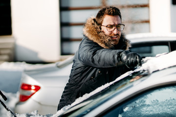 Caucasian man wearing warm jacket removes snow from vehicle, cleaning after snow blizzard