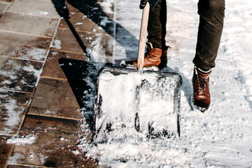 Man with snow shovel cleaning sidewalk during winter time. Close up on snow shovel