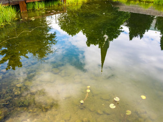 John the Baptist Church bell tower reflection on a public park pond water surface in Oberstdorf, Germany