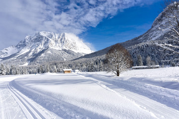 Fototapeta na wymiar Winter mountain landscape with groomed ski trails and blue sky in sunny day. Ehrwald valley, Tirol, Alps, Austria, Zugspitze Massif in background.
