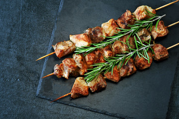 Juicy kebab with rosemary on a dark stone board.