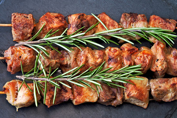 Juicy kebab with rosemary on a dark stone board.