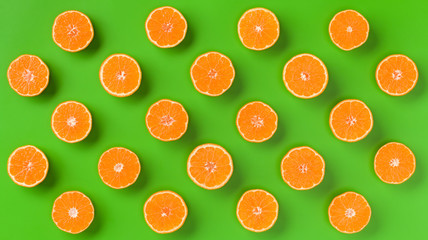 Fruit pattern of fresh orange slices on green background. Flat lay, top view. Pop art design, creative summer concept. Half of citrus in minimal style.