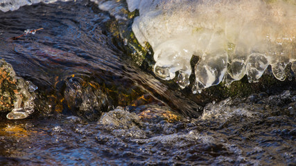water flowing around icy rocks in river during winter, closeup, river bank, beautiful