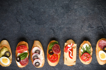 Open faced sandwich canape or crostini on dark stone background closeup. Top view.