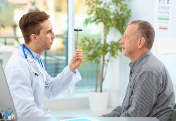 Doctor checking reflexes of mature patient in hospital - Powered by Adobe