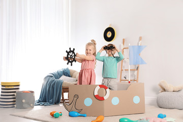 Cute little children playing with cardboard ship at home