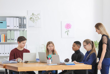 Group of teenagers doing homework with teacher in classroom