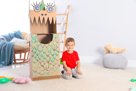 Cute little boy playing with cardboard dragon at home. Space for text