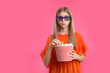 Fototapeta premium Emotional teenage girl with 3D glasses and popcorn during cinema show on color background