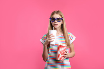 Fototapeta premium Emotional teenage girl with 3D glasses, popcorn and beverage during cinema show on color background