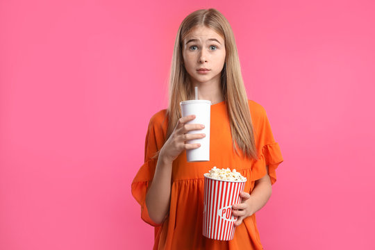 Emotional teenage girl with popcorn and beverage during cinema show on color background