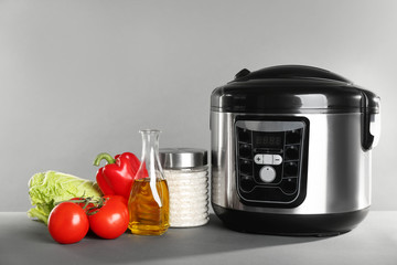 Modern multi cooker and products on table against grey background. Space for text