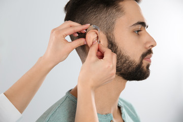 Fototapeta premium Otolaryngologist putting hearing aid in man's ear on white background