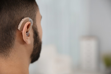 Young man with hearing aid indoors, closeup. Space for text