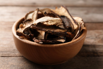 Bowl of dried mushrooms on wooden background, closeup