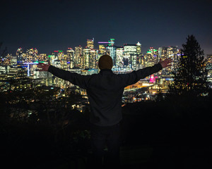 Happy Man Standing on Cliff Over City Lights Bokeh with Arms Out