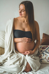 Attractive pregnant woman is sitting in bed and holding her belly. Last months of pregnancy.