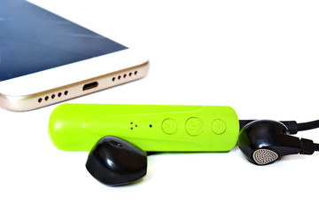 Green plastic Bluetooth adapter with connected black earphone for wireless connection to media audio devices on background of modern smartphone. Isolated. Face side