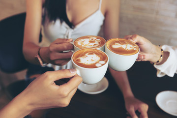 Group of friends cheers with latae cup in cafe bar with phone on table sitting intdoor at cafe -...